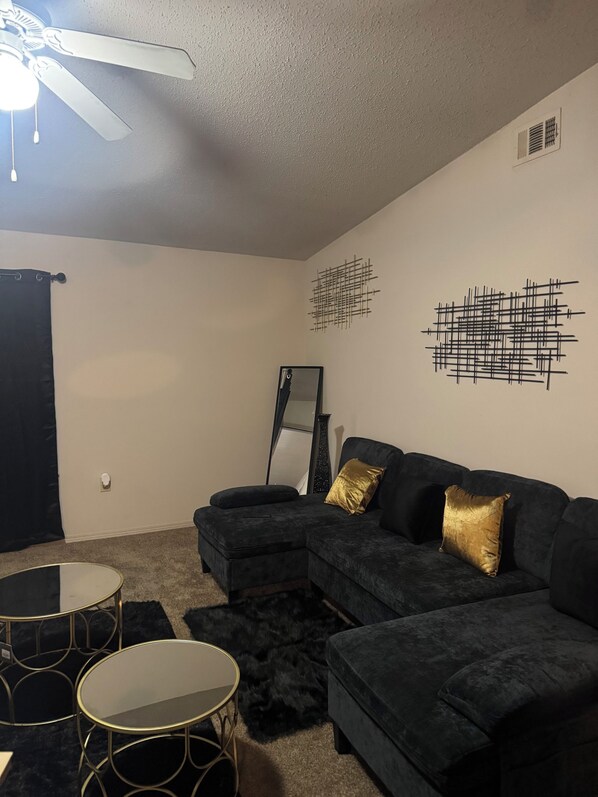 A living room with a dark-colored sectional sofa, a round coffee table, a black-framed mirror, and abstract wall art.