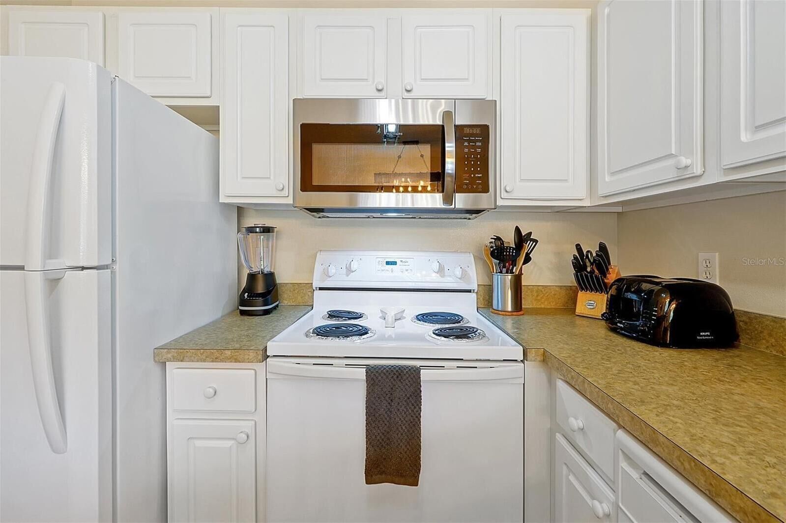 A kitchen with white cabinets, a microwave, a stove, a toaster, and a blender.