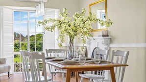Een eethoek met een houten tafel voor zes personen, witte stoelen en een vaas met witte bloemen.
