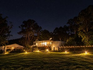 A house with a large open porch and a covered outdoor area, surrounded by trees and a well-lit lawn. - Private Farmstay with Pool & Animals (Dooralong)