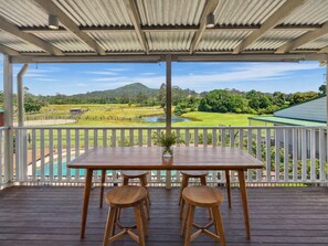 A wooden deck with a table and stools, overlooking a golf course and a body of water. - Private Farmstay with Pool & Animals (Dooralong)