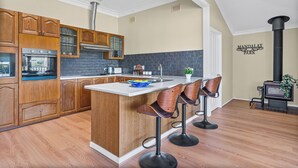 Een keuken met houten kasten, een centraal eiland met barkrukken, een fornuis en een zwart betegelde achterwand.