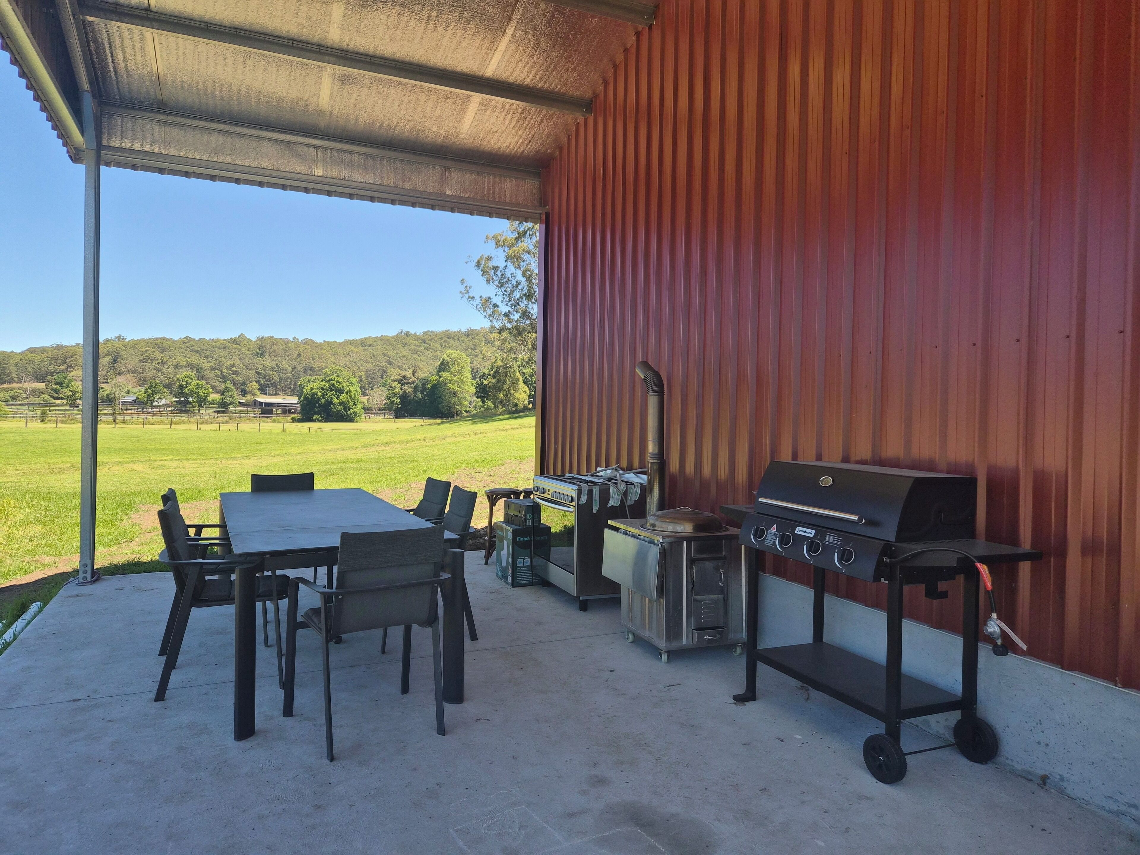 An outdoor patio with a grill and seating area, overlooking a green field.