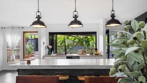 Eine moderne Küche mit Marmorarbeitsplatte, Holzbarhocker und Pendelleuchten.