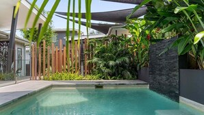 Ein Swimmingpool mit einer Steinmauer und tropischer Bepflanzung.