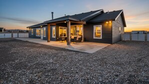A modern house with a covered patio, large windows, and a gravel driveway.