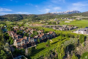 Un quartier résidentiel avec des maisons et un grand immeuble, entouré de collines verdoyantes et de montagnes.