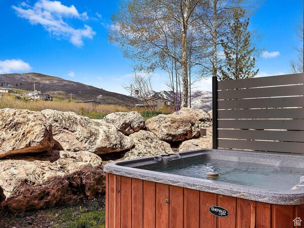 Un jacuzzi con revestimiento de madera y una tapa de piedra, rodeado de rocas grandes y una cerca de madera.
