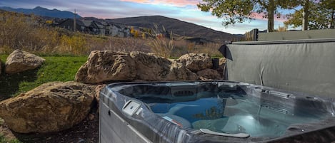 Un bain à remous dans un jardin, avec une vue panoramique sur les montagnes et un arbre.