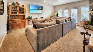 A cozy living room with a large sectional sofa, a wooden entertainment unit, and a stone fireplace. - Ski Townhome: 3 Resorts, Hot Tub, Pool (Huntsville)