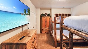 Een kamer met een televisie waarop een strand te zien is, stapelbedden, een houten kast en een klein tafeltje.