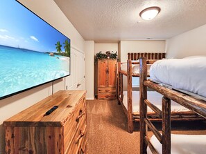 Habitación con televisión mostrando una playa, literas, un armario de madera y una mesita.