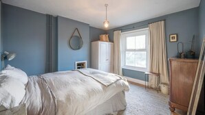 Um quarto com cama, guarda-roupa, espelho, janela com cortinas e luminária pendente.