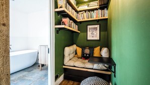 Uma casa de banho compacta com uma banheira branca, parede verde e área de estar embutida com estantes acima.