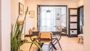 Uma sala de jantar com uma mesa comprida e cadeiras, uma planta em vaso e vista para outro cômodo.