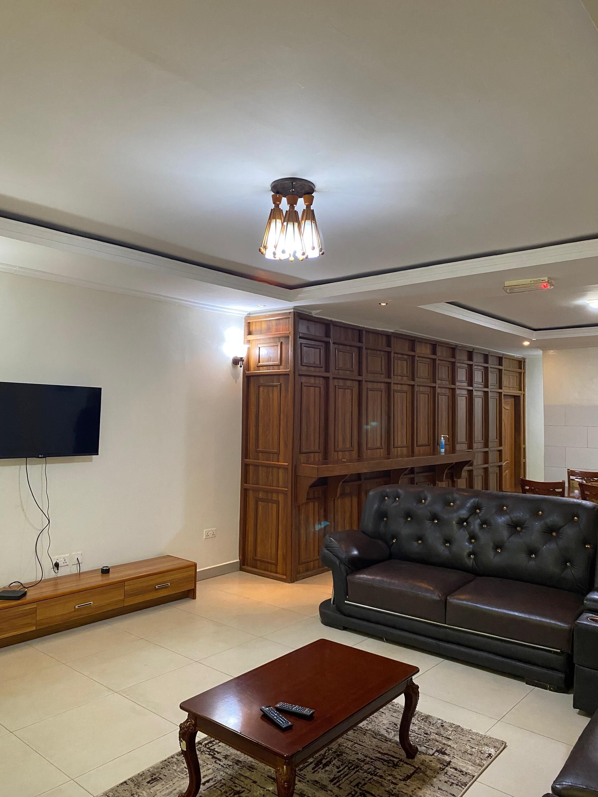 Een woonkamer met een flatscreen televisie, een leren bank, een houten kast en een salontafel.