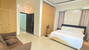 A hotel room with a bed, a chair, and a wardrobe. - KIGALI QUEENS HOME AND APRTMENTS (Kigali)