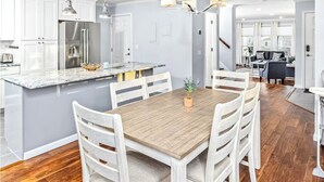 A modern kitchen with white cabinets, a stainless steel refrigerator, and a wooden dining table with white chairs. - Spacious Home • Hot Tub • Sleeps 24 • Near Airport (Anchorage)