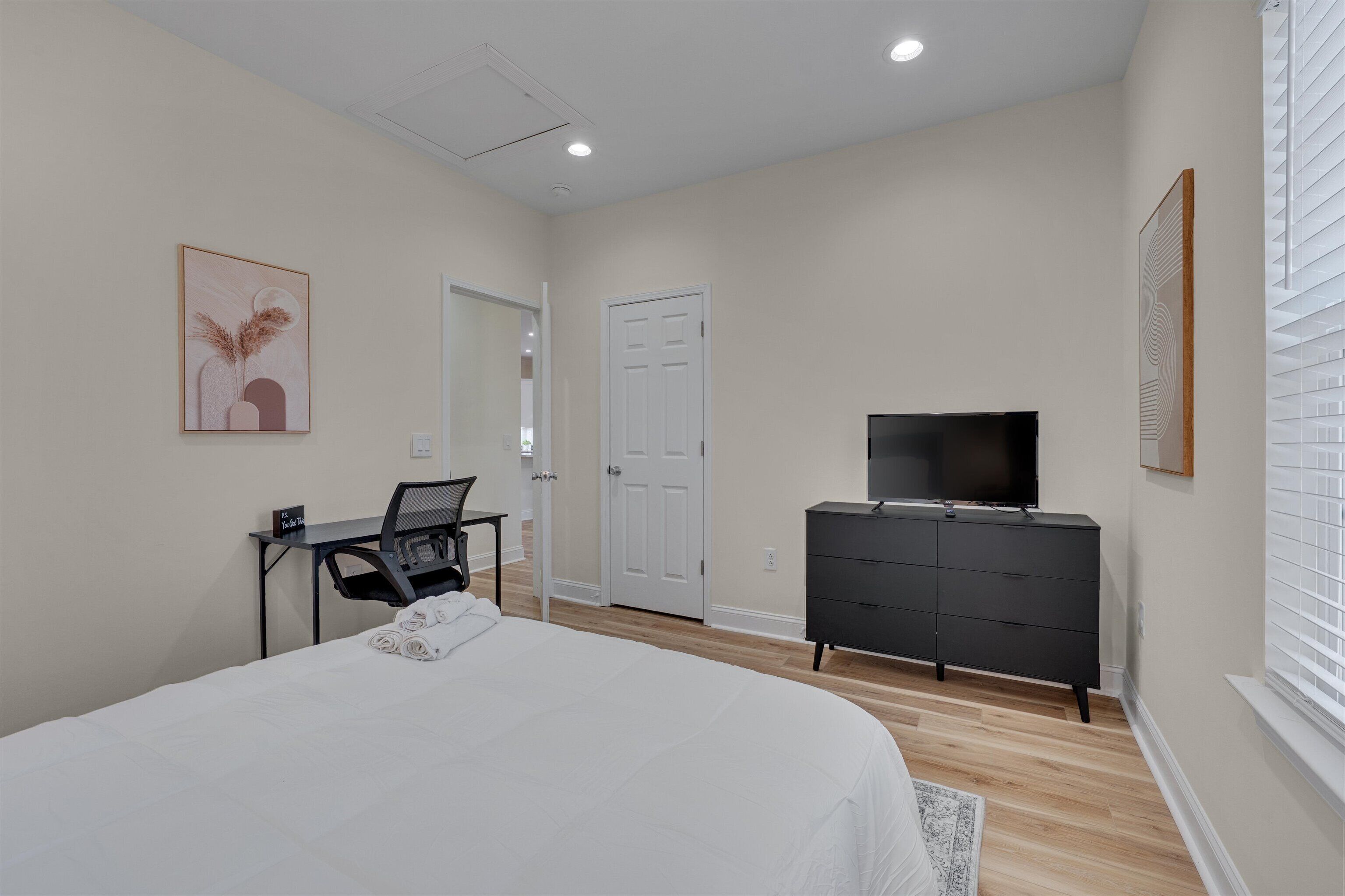 A hotel room with a bed, a desk with a chair, a television on a dresser, and a door.