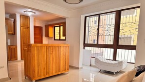 Ein geräumiger Wohnbereich mit einem Holzschrank, einem weißen Sofa und einem großen Fenster mit dekorativen Eisengittern.