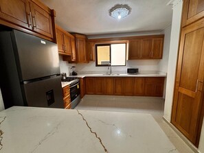 A kitchen with wooden cabinets, a refrigerator, a stove, a microwave, and a window. - in-charming Santiago, Rep. Dom. Amazing Wifi and AC (Santiago de los Caballeros)