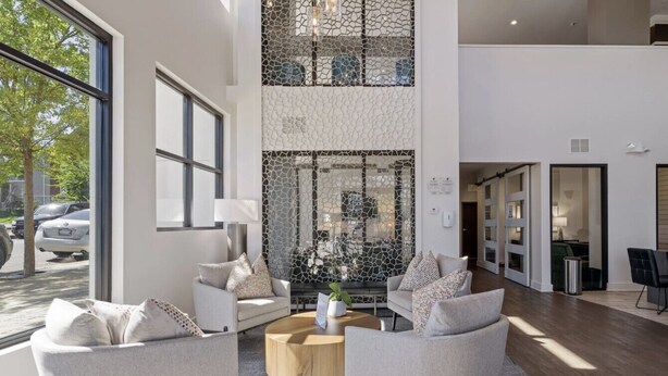 A spacious lobby with a high ceiling, large windows, and a central seating area with two sofas and a round coffee table. - Luxury Studio with Balcony and Makeup Room (Nashville)