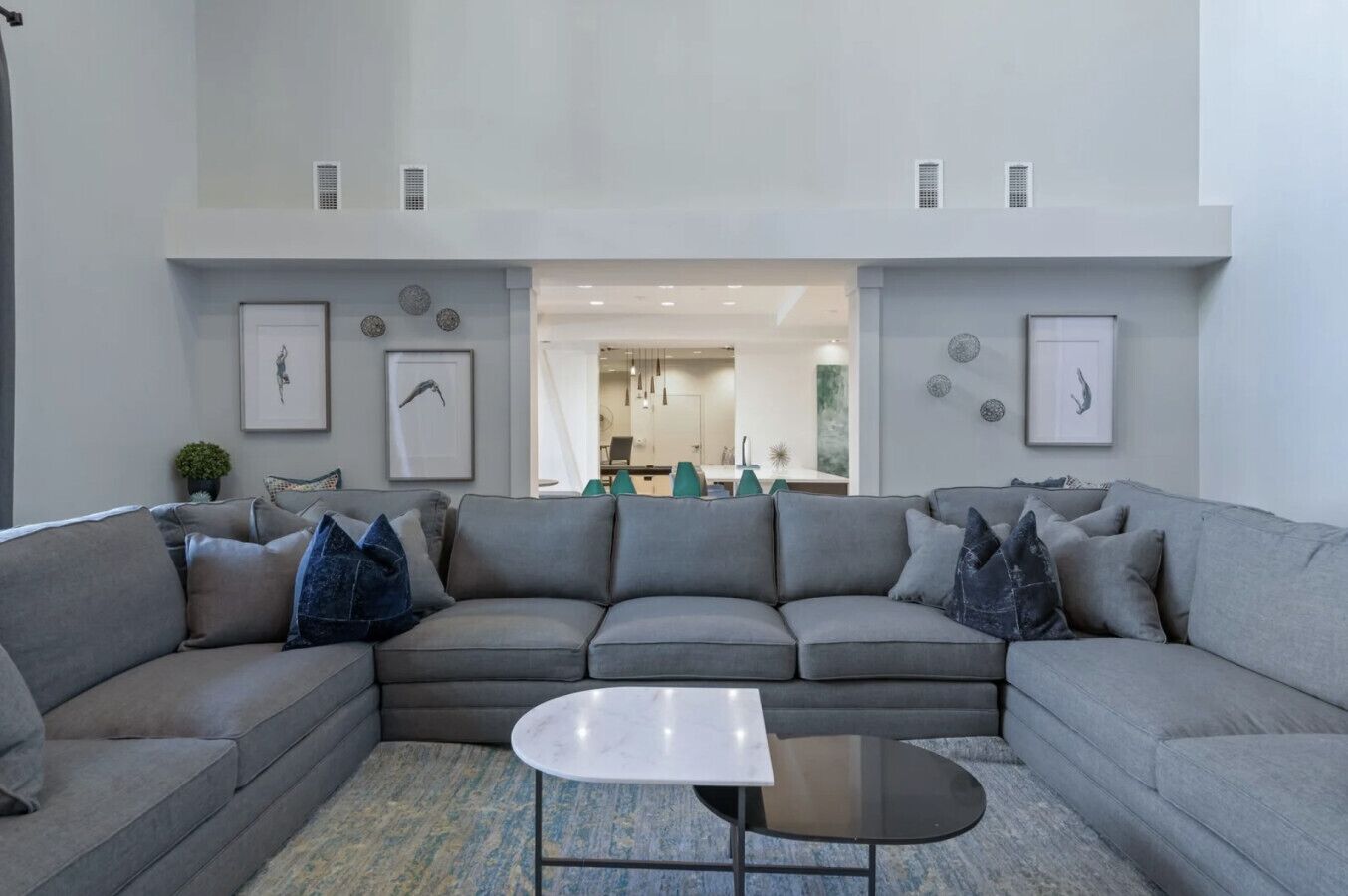 Uma sala de estar moderna com um sofá modular cinza, uma mesa redonda pequena e vista para a sala de jantar.