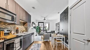 A modern kitchen with dark cabinets, a microwave, and a wooden countertop. There is a dining area with a table and chairs, and a large window in the background. - Luxury Studio with Balcony and Makeup Room (Nashville)