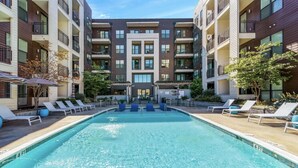A swimming pool surrounded by lounge chairs and a multi-story building with balconies. - Luxury Studio with Balcony and Makeup Room (Nashville)