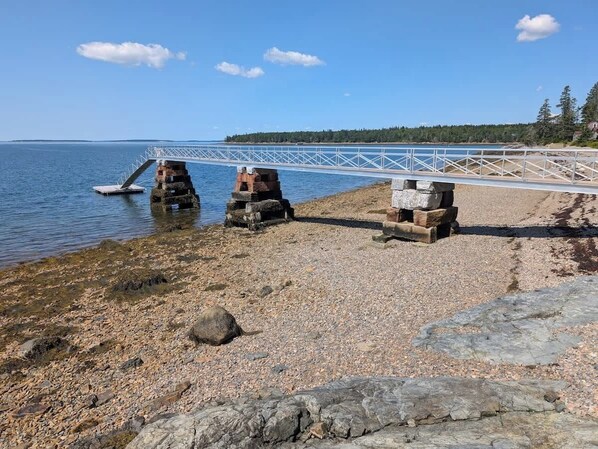 A rocky shoreline with a white bridge over water, a clear sky, and distant trees. - Boat Builders House - Oceanfront Acadia Getaway (Tremont)