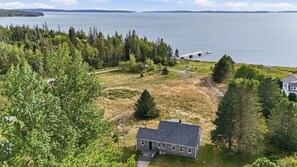 A house with a stone exterior, a front porch, and a view of a lake and bridge. - Boat Builders House - Oceanfront Acadia Getaway (Tremont)