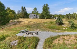 A house with a gravel driveway leading to a picnic area with outdoor seating and a fire pit. - Boat Builders House - Oceanfront Acadia Getaway (Tremont)