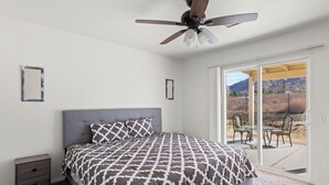 Ein Schlafzimmer mit Bett, Nachttisch, Deckenventilator und einer Glastür, die auf eine Terrasse im Freien führt.