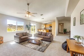A spacious living room with a large window, a ceiling fan, and a view of a desert landscape. - Joshua Tree Home • Fire Pit • Near Natl Park (Joshua Tree)