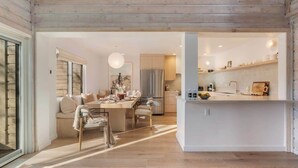 A modern kitchen with a central island, wooden ceiling, and a dining area with a sofa and chairs.