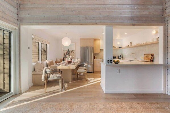 A modern kitchen with a central island, wooden ceiling, and a dining area with a sofa and chairs.