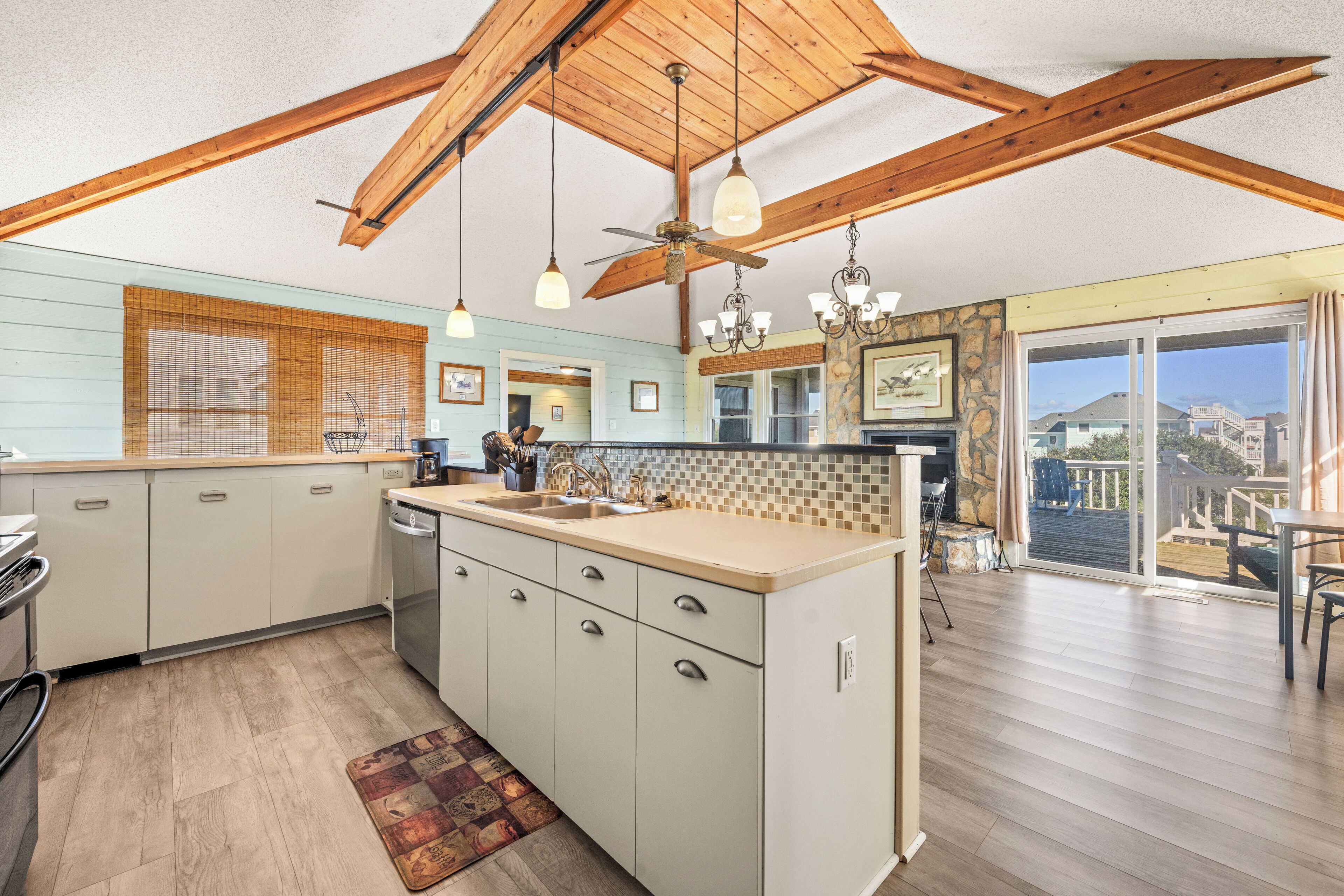 A spacious kitchen with a large island, wooden ceiling beams, and a view to a balcony.