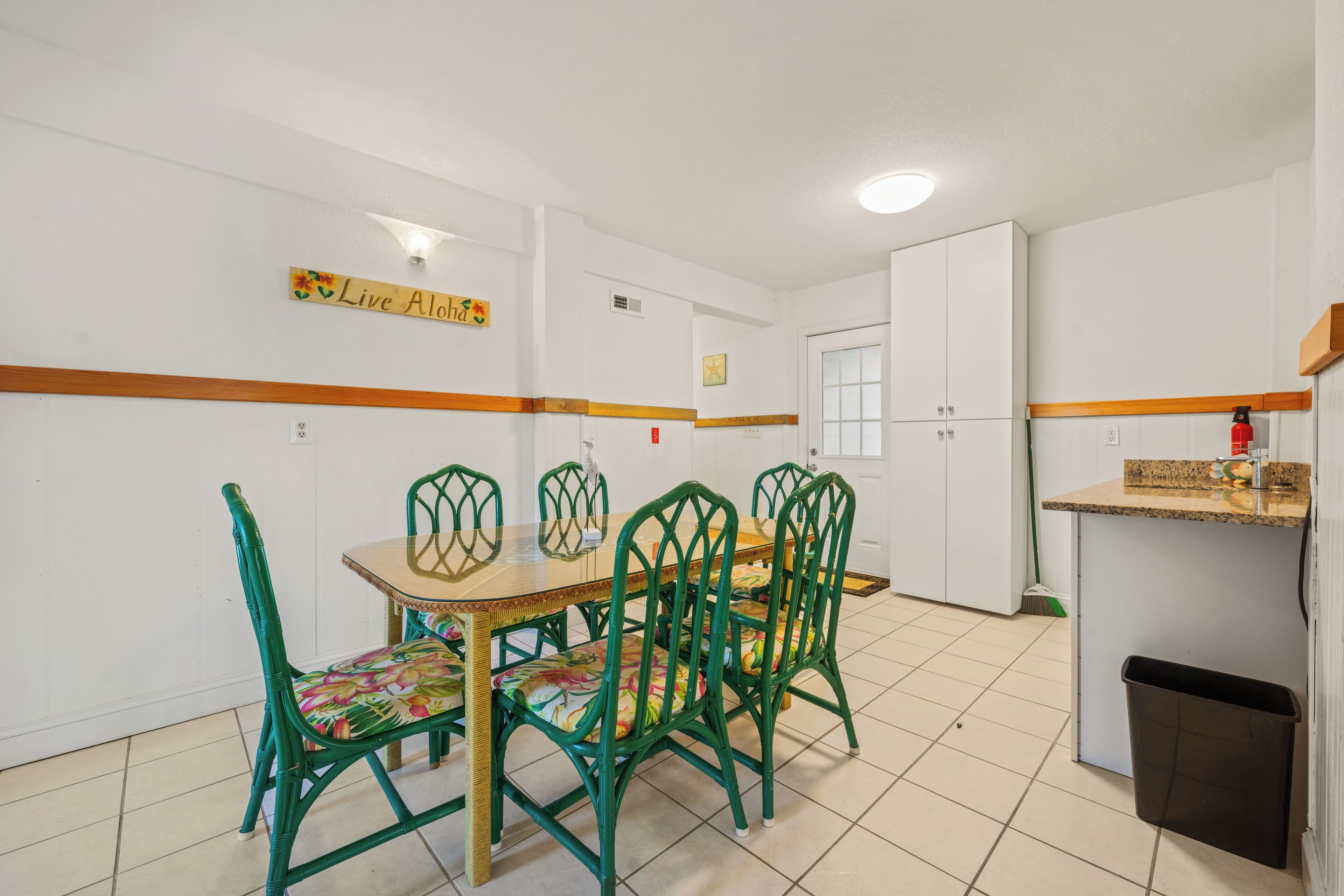 A dining area with a wooden table and green chairs, a kitchen area with cabinets and a countertop, and a sign on the wall that reads "Live Along".