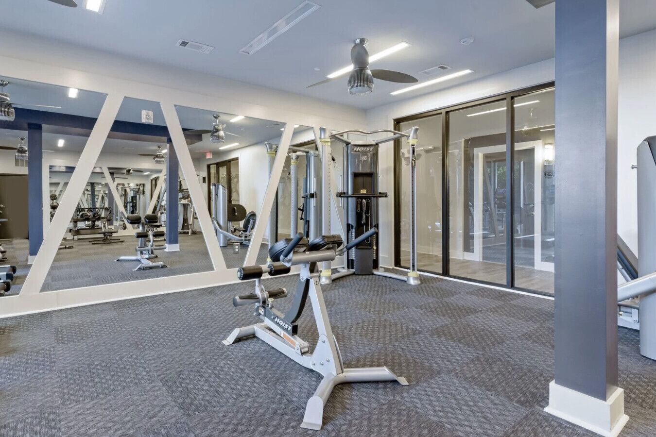 Un gimnasio moderno con paredes espejadas, ventiladores de techo y diverso equipamiento de ejercicio.