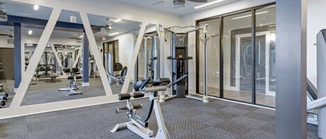 Un gimnasio moderno con paredes espejadas, ventiladores de techo y diverso equipamiento de ejercicio.