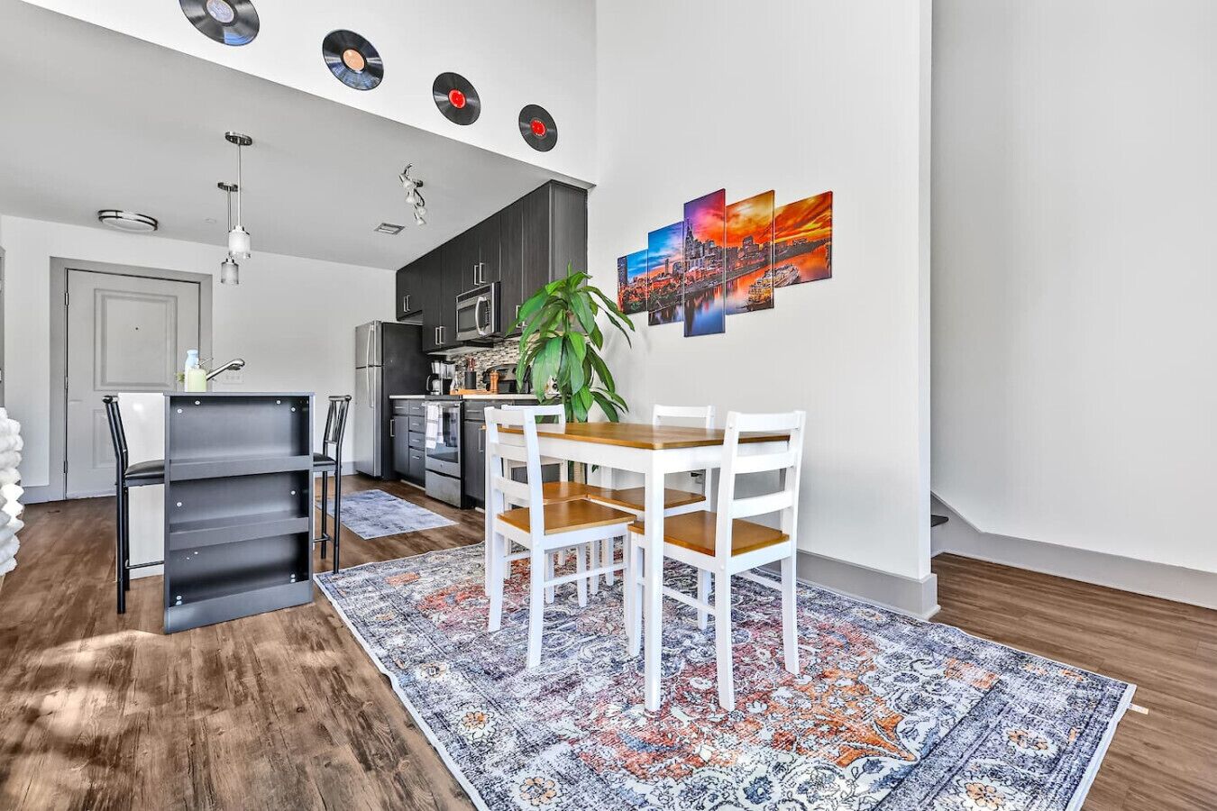 A modern kitchen with dark cabinets, a wooden dining table, and a patterned rug.