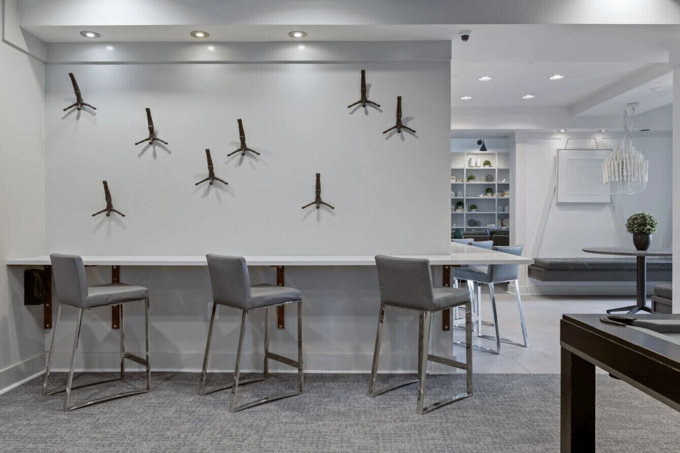 A modern interior with a bar area, grey chairs, a white counter, and a bookshelf.