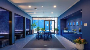 Eine moderne Hotelhalle mit dunklem Blauton, einer zentralen Sitzgruppe mit Tisch und Stühlen sowie Zimmerpflanzen.