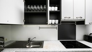 Une cuisine dotée d’un comptoir en granit, d’un évier en acier inoxydable, d’une cuisinière noire, d’armoires blanches et d’un meuble à vin intégré.
