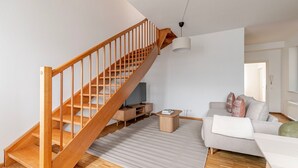 Un salon moderne avec un escalier en bois, un canapé gris, une petite table basse en bois et un téléviseur.