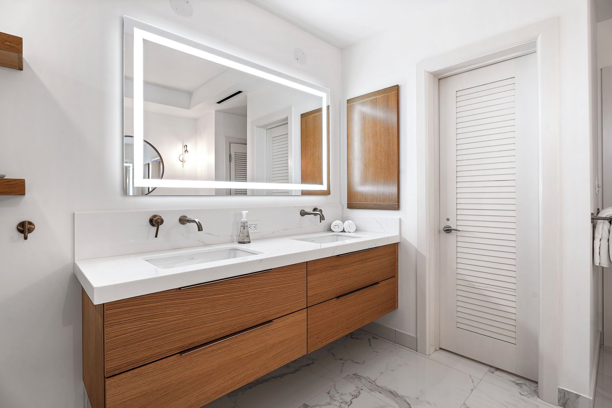 A bathroom with a large mirror, two sinks, wooden cabinets, and a white door.