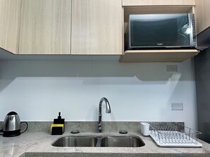 A kitchen with a stainless steel sink, a kettle, a microwave, and a dish rack. - Charming 1 Bedroom Apartment Unit in the Heart of The City. (Kingston)