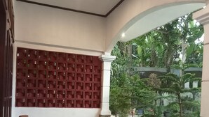 A room with a wooden chair, a potted plant, a red partition, and a view of greenery outside. - Pakemsari Resort Hotel (Pakem)