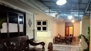 A spacious room with a marble floor, a dark wooden bench, a small table with a statue, and a dining area in the background. - Pakemsari Resort Hotel (Pakem)
