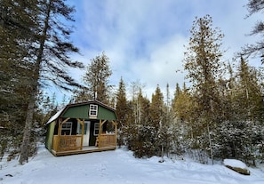 Une cabane dotĂ©e dâun porche, entourĂ©e dâarbres et de neige.